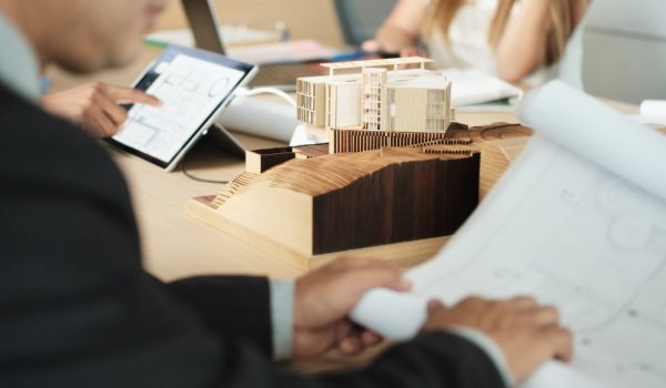 Business people working in modern office during conference. Architect and clients at meeting in executive room, showing housing plans and miniature house.